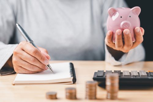 Hand mit Notizbuch und Sparschwein